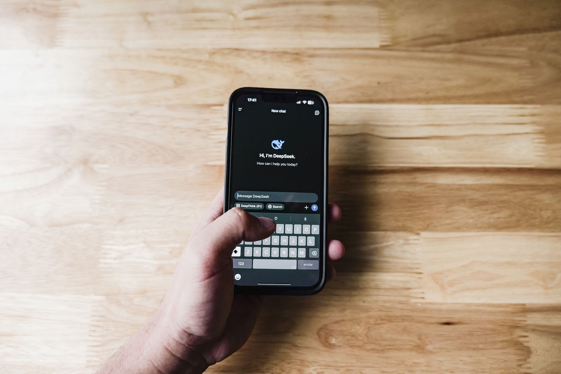 A person holding a smartphone at a kitchen table while choosing an AI assistant app.