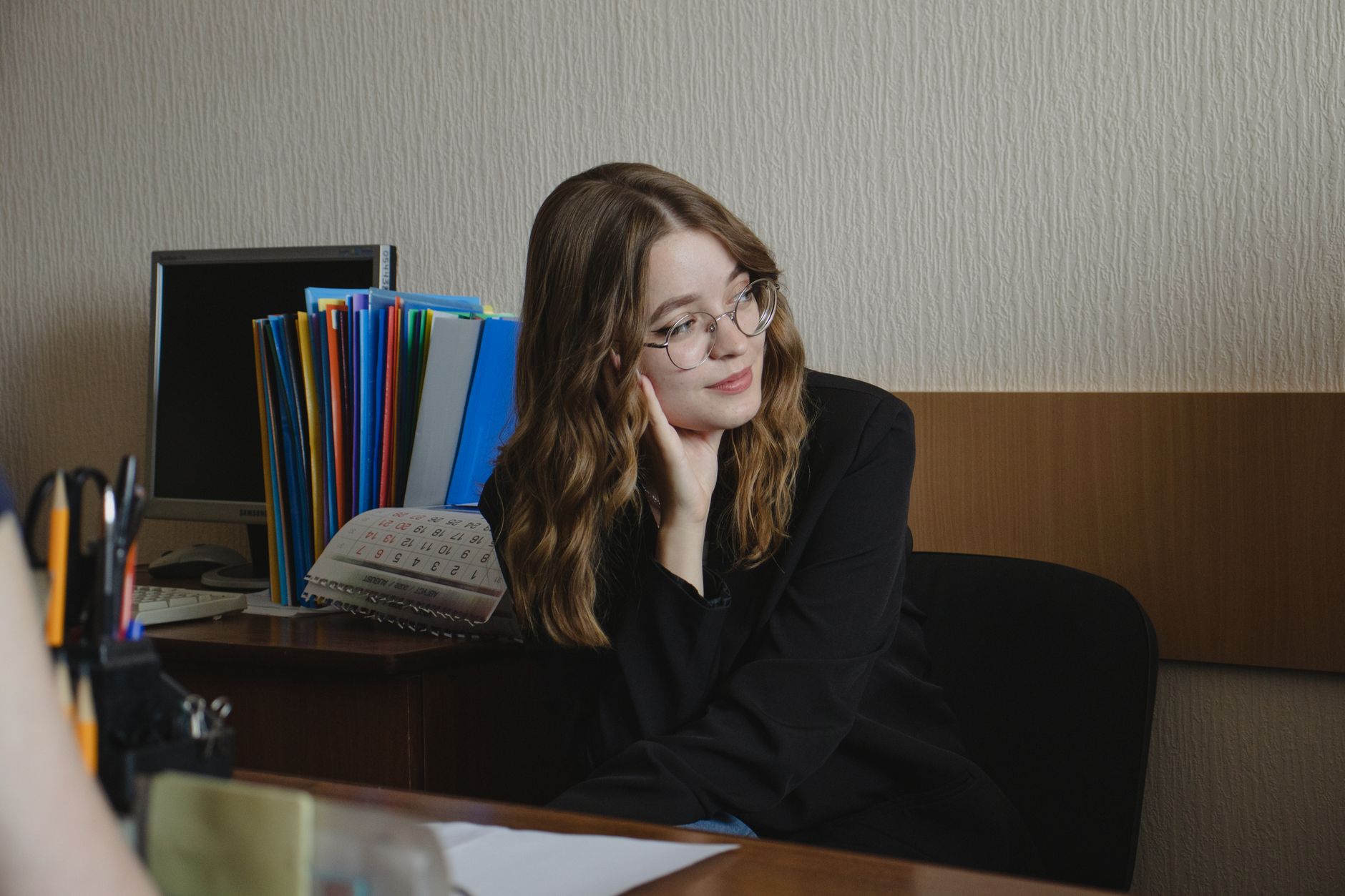 A student sits at a desk with a hand on their chin, looking thoughtful while studying with a laptop.