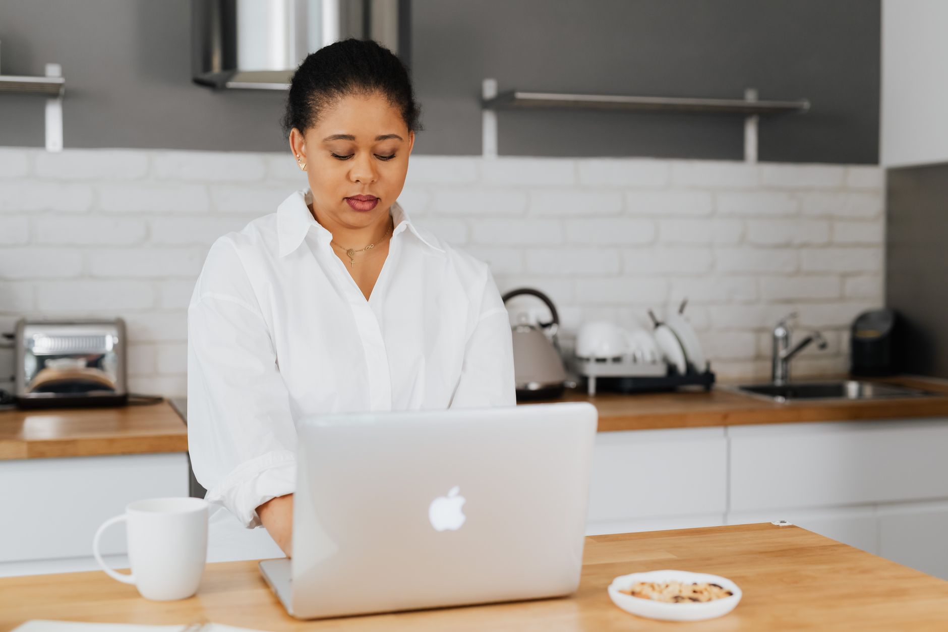 A person typing on a laptop at a kitchen counter with vegetables nearby.