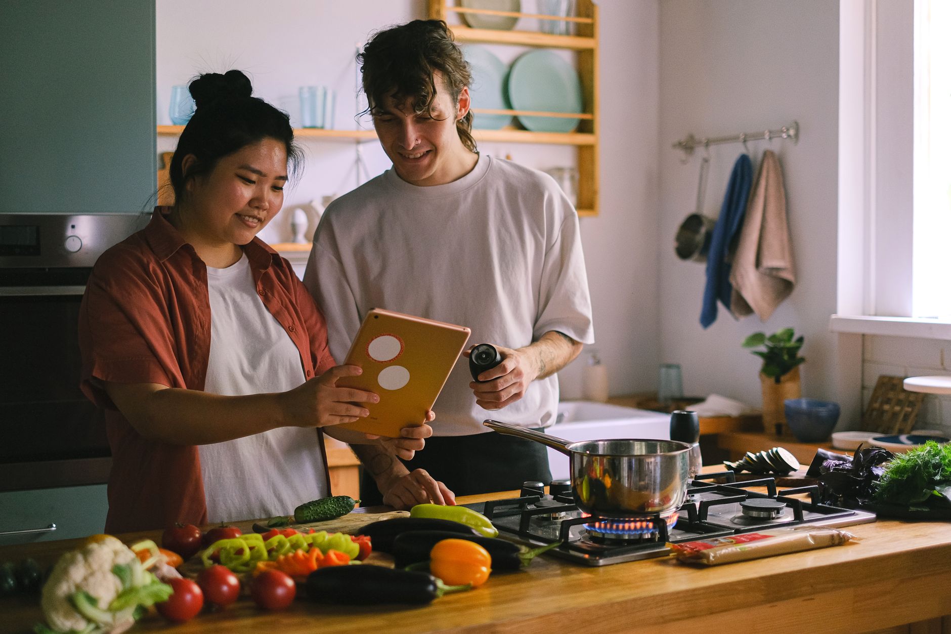 Family cooking together in kitchen while parent follows recipe on a tablet