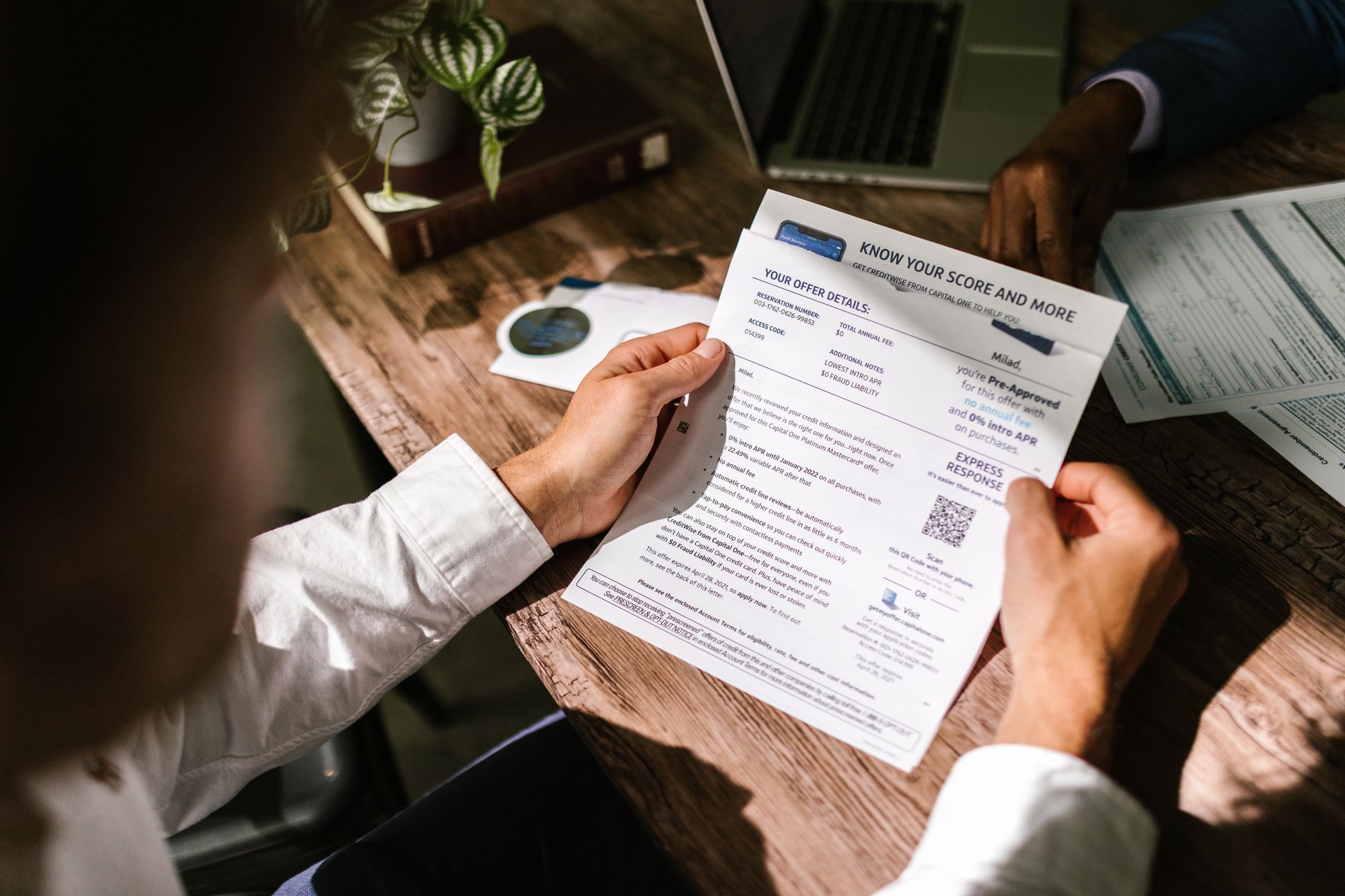 A person at a kitchen table reviewing printed bank statements next to a laptop