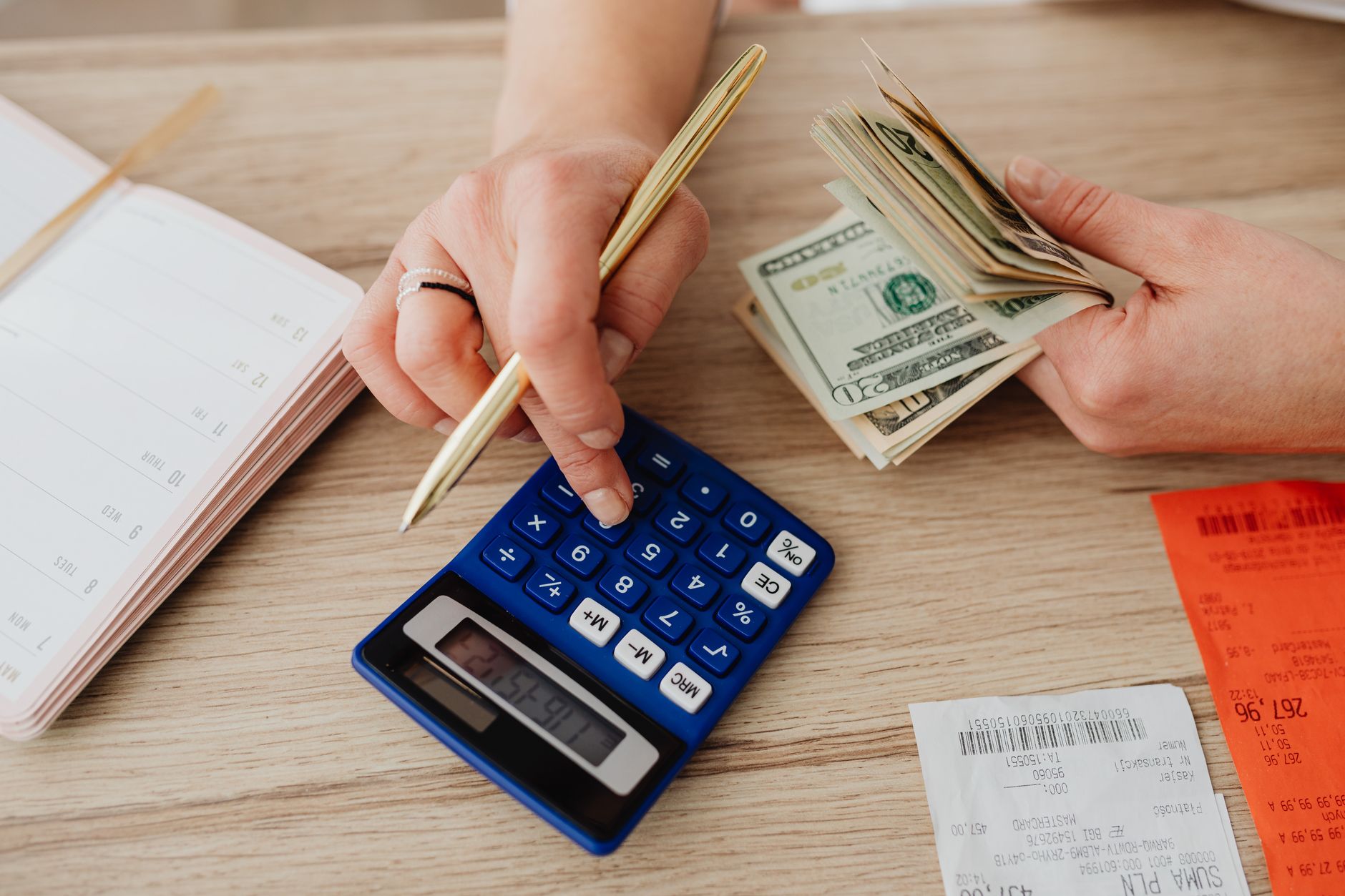 A person writing a monthly budget plan in a notebook with a calculator and laptop open
