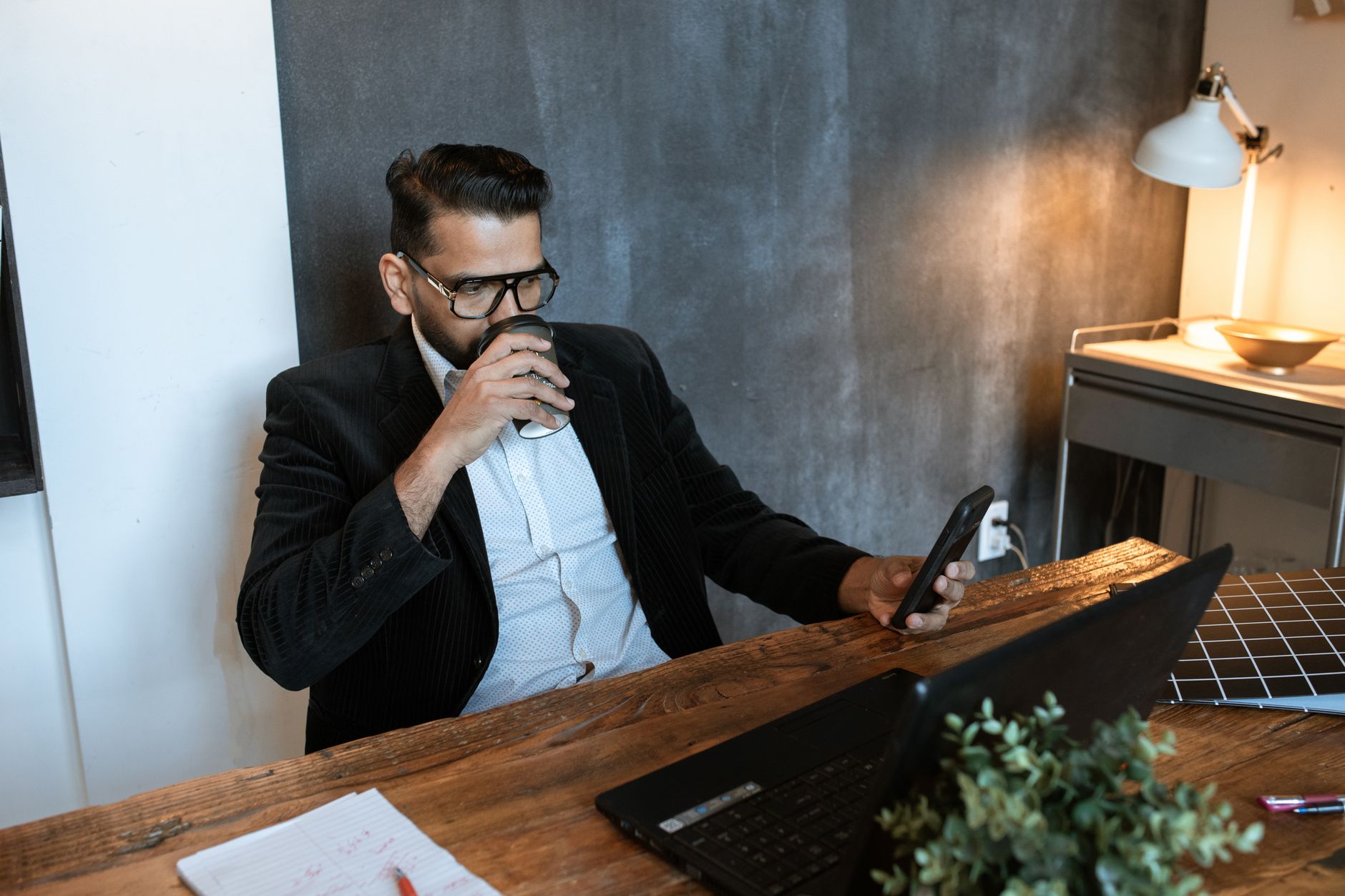 A person sitting on a couch checking a budget app on a phone while holding a coffee mug