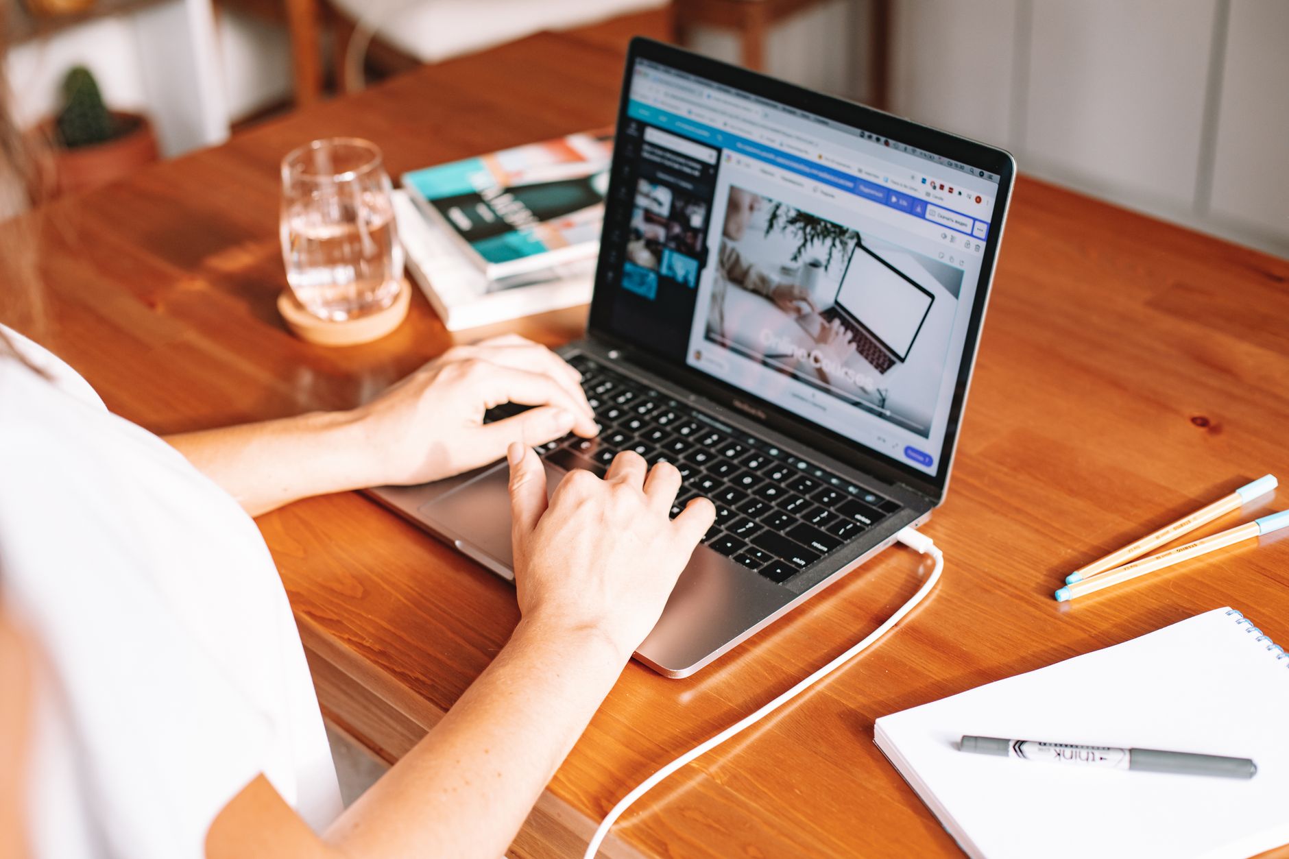 Person typing on a laptop at a tidy home desk with a notebook and coffee mug nearby.