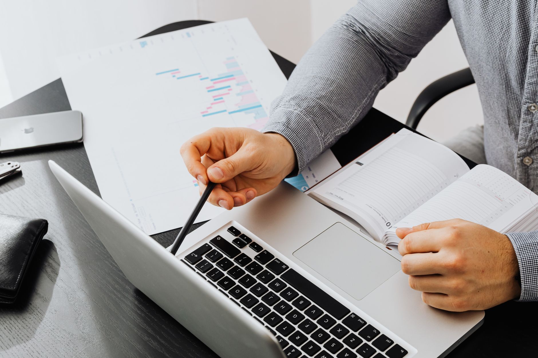 Person working in a bright office with a laptop, printed charts, and a notepad on the desk.