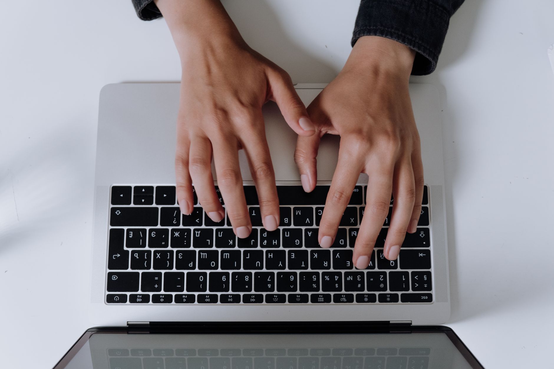 A person at a tidy desk types a redacted document into a chat window on a laptop, with a smartphone nearby.