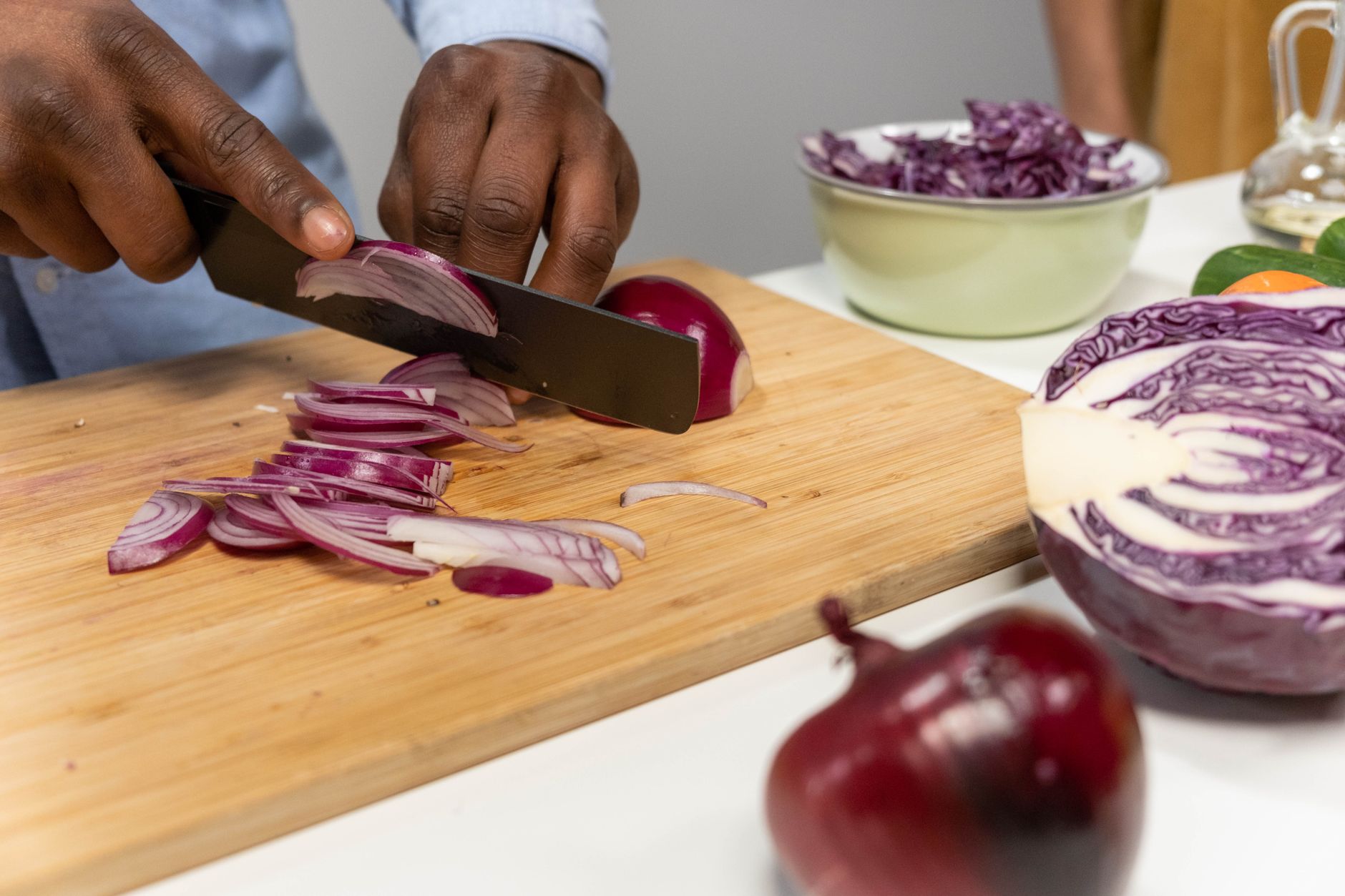A person chops vegetables on a cutting board in a bright kitchen with fresh ingredients like tomatoes and spinach on the counter.